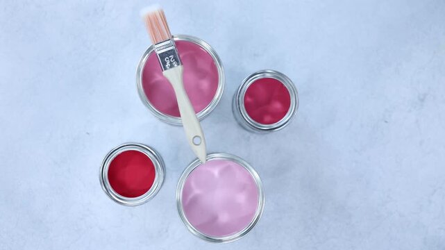 Cans with paint in shades of pink and brush on light grey table, flat lay. Camera moving in