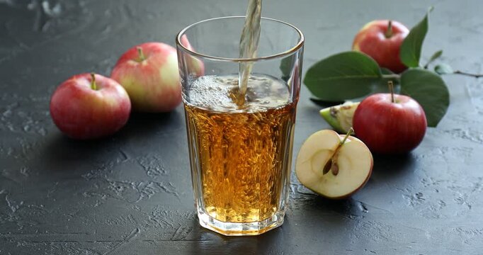 Pouring delicious apple juice into glass at grey textured table, closeup