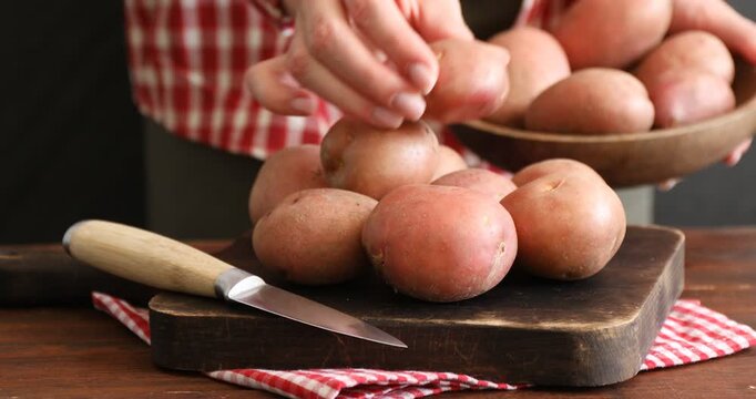 Woman putting ripe red potatoes onto board at table, closeup