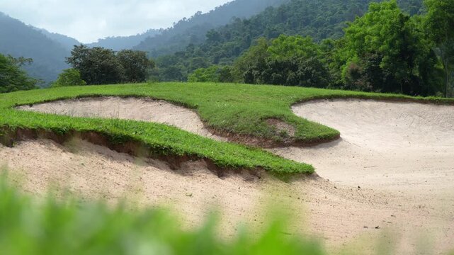 The sand trap area of ​​ golf course is background by mountains.