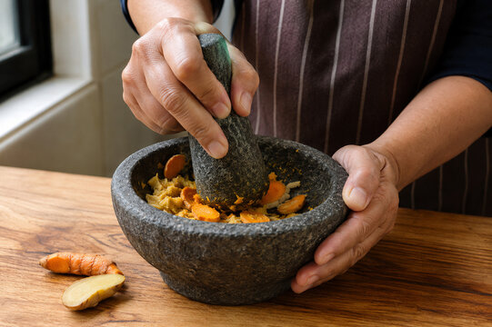 Malaysian Home Cook Grinding Fresh Turmeric and Ginger with Traditional Granite Mortar and Pestle