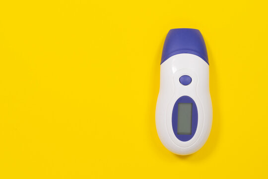 A blue and white infrared thermometer with a digital display lies on a yellow background with copy space, a concept of health monitoring and fever check.