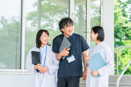 笑顔で会話しながら歩く3人の白衣姿,スクラブ姿の医療スタッフ