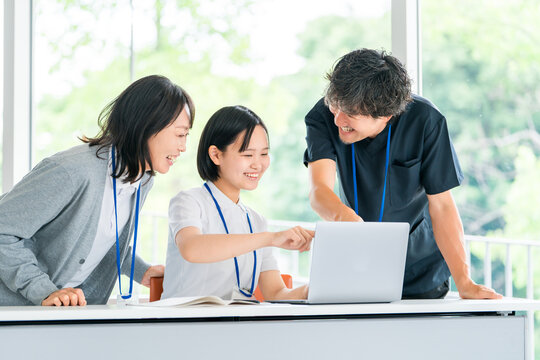 Male and female medical staff members are seen smiling and having a meeting around a computer.