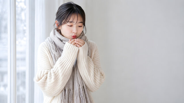 冬の室内で冷えた両手に息を吹きかけて温める若い日本人女性