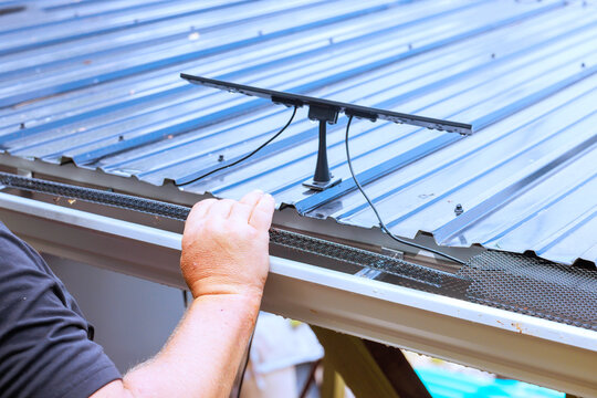 Construction worker attaches solar panel to metal roof while working outside.