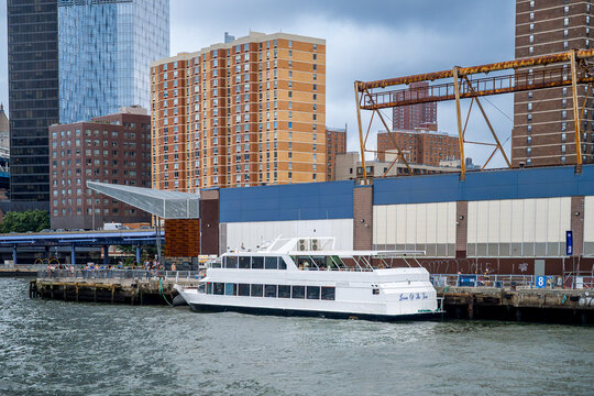 New York, USA, 5 Jule 2026 : White cruise boat moored at pier along East River in Manhattan. Passenger vessel docked near waterfront building with metal superstructure