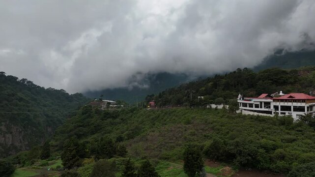 Drone rotates around its axis revealing cultivated mountain farms, green slopes and dramatic low clouds in Zunil, Quetzaltenango, Guatemala.