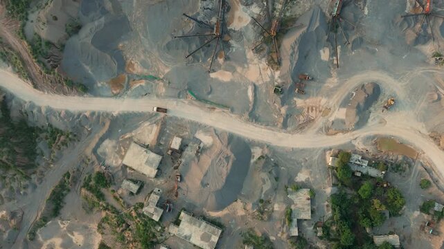 Top down drone shot of a heavy industrial dump truck driving along a dusty dirt road through an active stone crushing quarry surrounded by sorting machinery and gravel piles