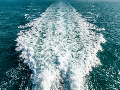 White boat wake trail on deep blue ocean water surface view from above