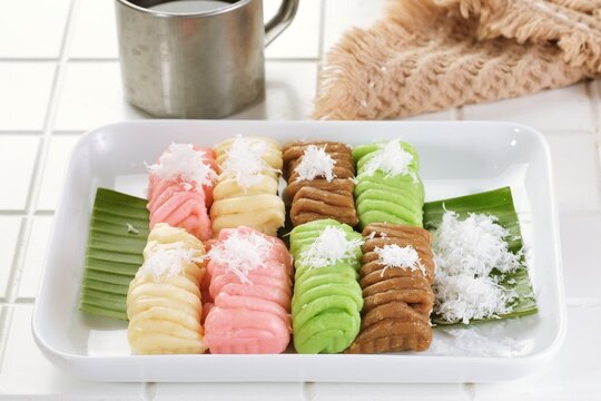Colorful getuk lindri with grated coconut served on a banana leaf and white plate, accompanied by a beverage for a traditional Indonesian tea time concept.
