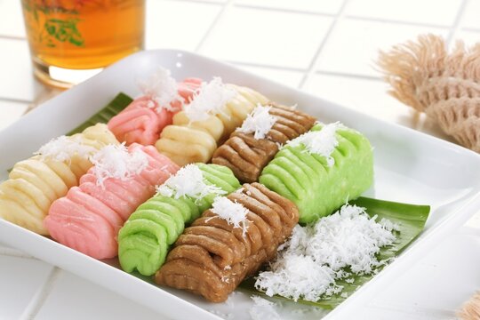 Colorful getuk lindri, a traditional Indonesian cassava snack, served with grated coconut on a white plate over a banana leaf with rustic food styling.