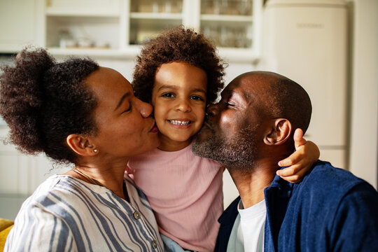 Parents kiss their smiling child in the home kitchen