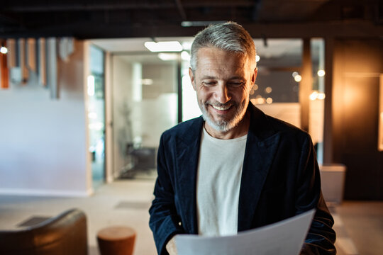 Smiling mature businessman reading document in modern office
