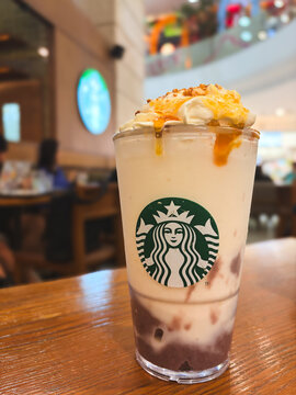 Bangkok, Thailand - September 3, 2026: Close up of a Starbucks blended Frappuccino beverage with whipped cream, caramel drizzle, and nut topping on a wooden table in a cafe.