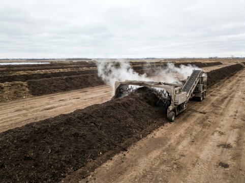 Industrial compost turner processing steaming organic matter in long dark windrows
