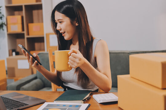 Startup SME small business entrepreneur of freelance Asian woman wearing apron using laptop and box to receive and review orders online to prepare to pack sell to customers, online sme business ideas.