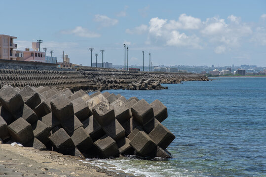 快晴の空と遠くに街灯のある公園が見える消波ブロックの並ぶ防波堤の海岸