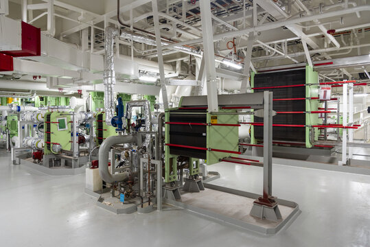 View from a platform inside the engine room of a modern commercial vessel, showing several cooling water heat exchangers serving the main engine and auxiliary shipboard systems.