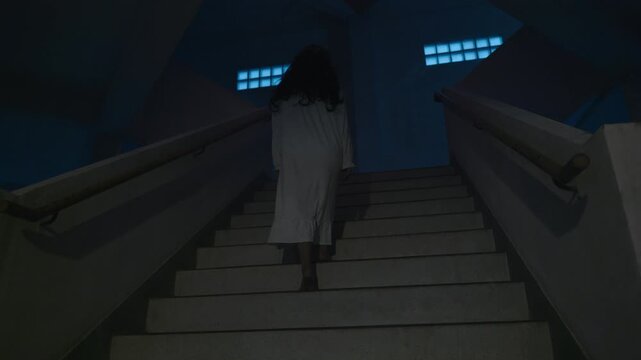 Scary halloween ghost ascends dark stairs, wears white costume, long black hair, creepy night, mysterious building, spooky dark atmosphere, horror concept day dead night.