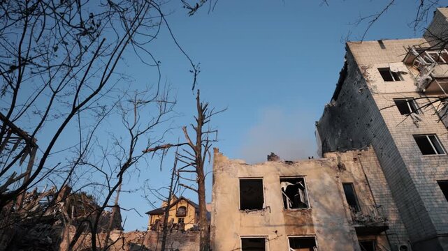 War-torn city, Rising smoke, Conflict damage. Row of heavily damaged apartment blocks shows shattered windows and smoke from recent destruction.