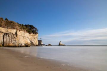 Fototapeta premium Scenic Coastal Cliff and Calm Sandy Beach Under Blue Sky