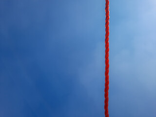 Red plastic rope hanging vertically with copy space over a bright blue sky. © Day Dreamer 59