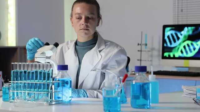 Tired female chemist working late in a medical laboratory analyzing a sample with a microscope while developing a new drug for treating disease or a new vaccine