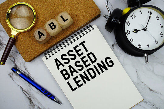 ABL Asset Based Lending text written on notepad with magnifying glass and alarm clock on marble background
