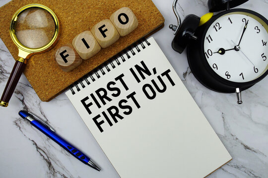 FIFO First-In, First-Out text written on notepad with magnifying glass and alarm clock on marble background
