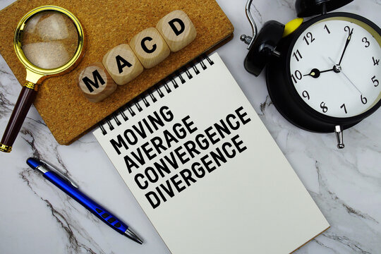 MACD Moving Average Convergence Divergence text written on notepad with magnifying glass and alarm clock on marble background