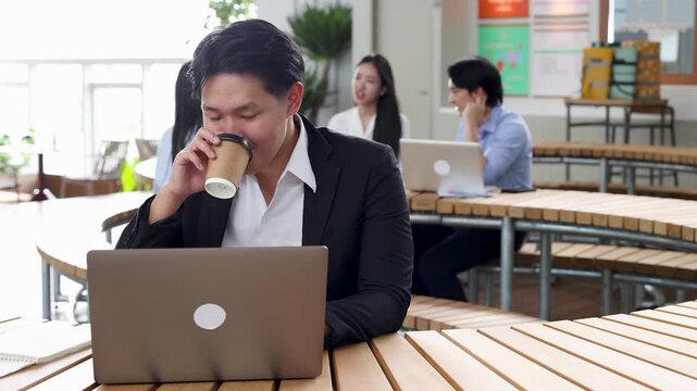 Asian Businessman Drinking Coffee While Working on Laptop in Modern Office