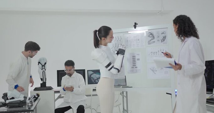 Engineers presenting and testing robotic arm at technical drawing board in white robotics lab