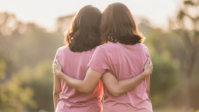 Two women hugging from behind in pink t-shirts, female friendship and support concept, outdoor park background with warm sunset light