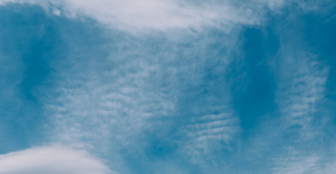 Wave-like cloud pattern in bright blue sky, abstract weather background.