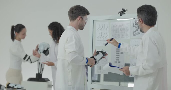 Engineers presenting and testing robotic arm at technical drawing board in white robotics lab