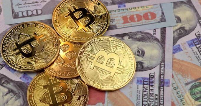 Horizontal detailed view of hand placing shiny golden bitcoin coin diagonally across spread hundred US dollar banknotes in macro orientation.