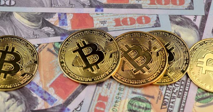Horizontal extreme macro view of glowing bitcoin cryptocurrency coin being stacked on top of hundred dollar cash banknotes on a dark surface.