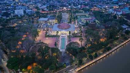 Fototapeta premium Illuminated Sabilal Muhtadin Mosque surrounded by greenery and river at dusk in Banjarmasin