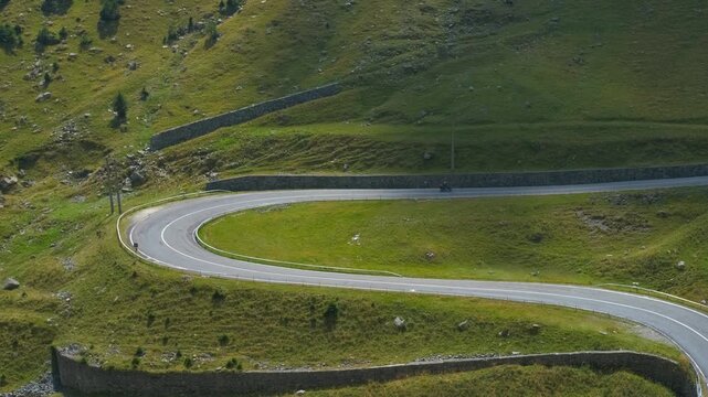 Motorcycle driving on a winding mountain road. Solitary motorcyclist riding a scenic, twisting mountain pass through a lush green landscape. The aerial view highlights the hairpin turns