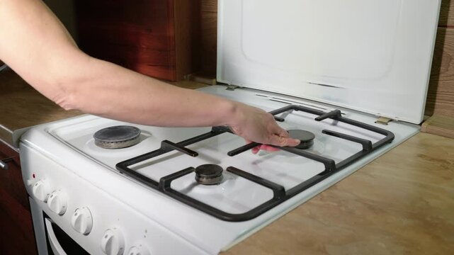 Person installing grates on a white gas stove top. Close-up view of a person's hands installing the cast iron grates on a clean white gas stovetop after washing, preparing the kitchen appliance