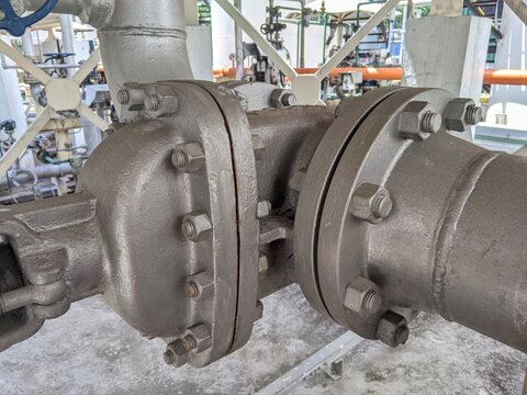 Close-up view of heavy industrial pipe flange joint with bolts and valve in a processing plant