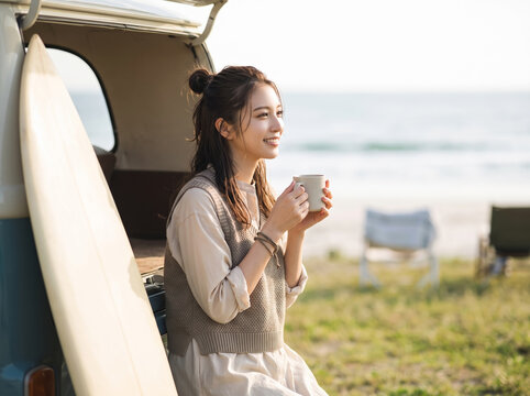 海辺のキャンピングカーのそばでコーヒーを飲みながらくつろぐ女性