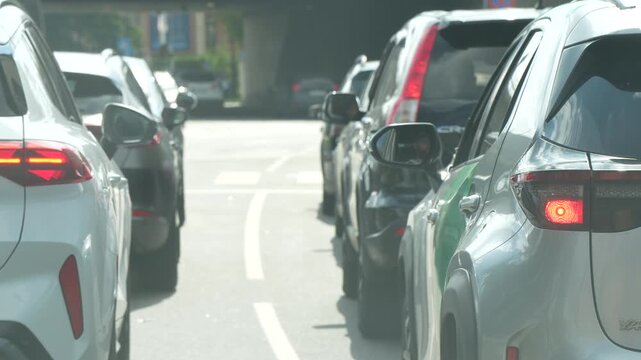 A queue of cars waits with brake lights glowing at a city intersection, drivers stopped in what has become typical urban rush-hour traffic today again.