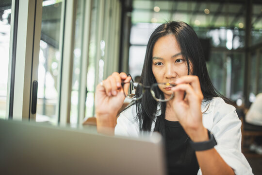 Tired woman removing glasses and rubbing her eyes while working on a laptop, illustrating eye strain, visual fatigue, prolonged screen time, stress and digital work.