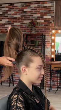 Hairdresser styles long hair into a high ponytail with braids in a beauty salon, professional hairstyling, elegant beauty and creative hairstyle.