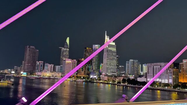 Nighttime view of Ho Chi Minh City skyline along the Saigon River, featuring illuminated skyscrapers, modern architecture, city lights, and reflections on the water. Atmospheric urban footage showcasi