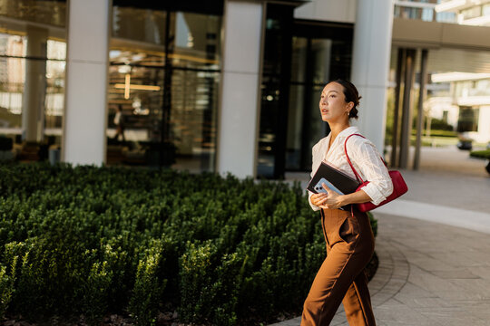 Korean woman in formal attire walks confidently through a modern urban setting