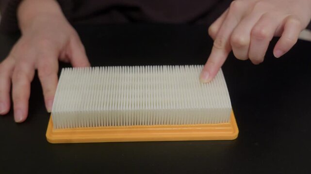 Close up of hands examining corrugated HEPA air filter with yellow plastic frame against dark background, testing filtration surface quality. With original sound captured.