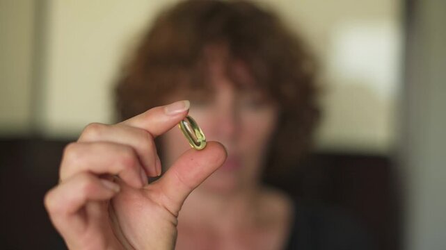 Woman with curly hair displays omega-3 supplement capsule in hand, emphasizing its significance for health in a well-lit indoor environment